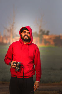 Portrait of young man holding camera while standing outdoors