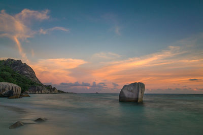 Rock formation in sea at la digue island against sky during sunset