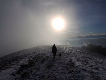 Rear view of silhouette man walking on snow covered landscape