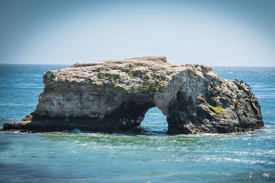 Rock formation by sea against clear sky