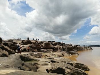 People on rocks by sea against sky