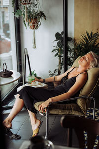 Blond woman in black dress sitting alone in cafe in relaxed position