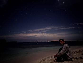 Full length of man sitting on land against sky at night
