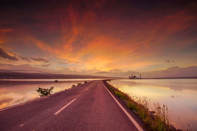 Road by sea against sky during sunset