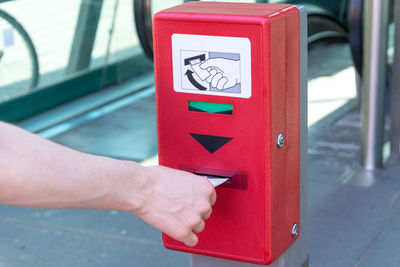 Cropped hand taking ticket from red machine on footpath