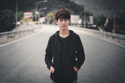 Portrait of young man standing on road in city