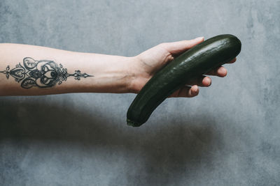 Cropped hand holding cucumber against wall