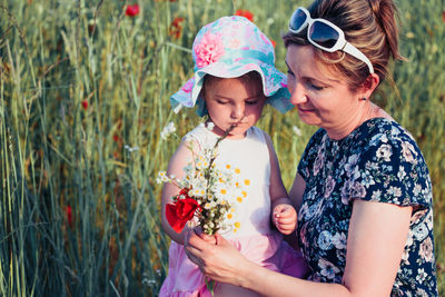 Girl holding flower by mother on grass