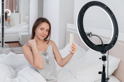 Female blogger recording vlog video on smartphone at home online influencer on near bed. streaming