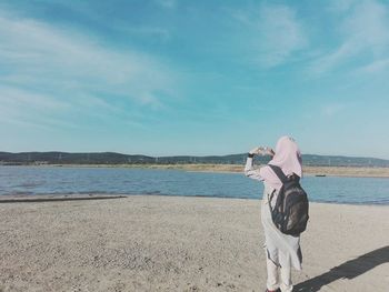 Rear view of woman with backpack looking at sea against sky