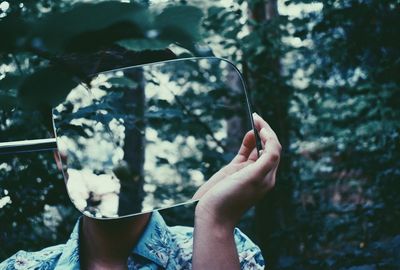 Woman holding mirror while standing in forest