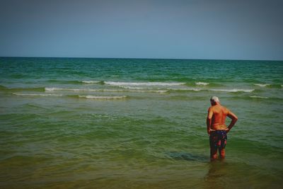 Rear view of shirtless man standing on beach against clear sky