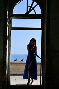 Full length of woman standing by door against sea