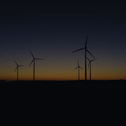 Silhouette wind turbines on field against sky during sunset