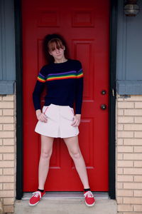 Portrait of young woman standing against red door