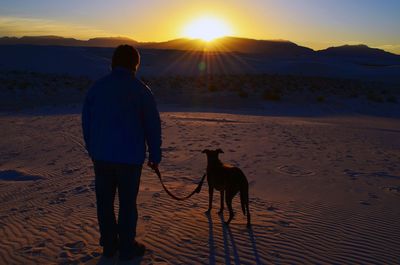 Rear view of man with catahoula leopard dog standing at white sands national monument during sunset