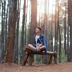 Happy teenage boy sitting on log in forest