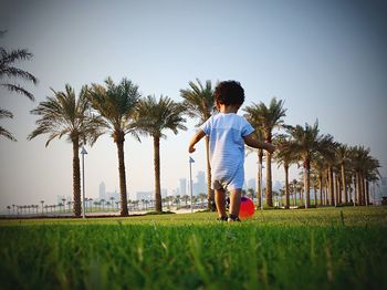Boy playing with ball on field against palm trees