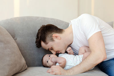 Young father kissing baby lying on sofa