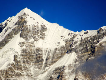 Low angle view of snowcapped mountains against clear blue sky