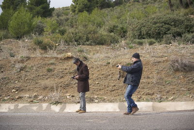 Full length of men holding camera standing on road against trees