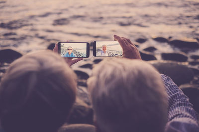 Rear view of couple taking selfie from mobile phones at beach