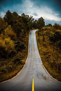 Empty road by trees against sky