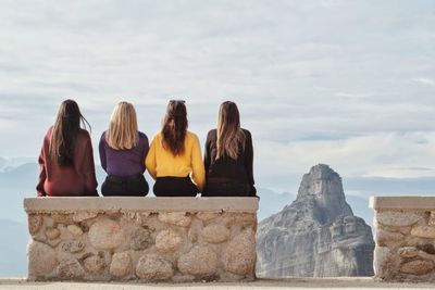 Rear view of people sitting on rock against sky