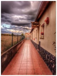 Walkway leading towards building against cloudy sky