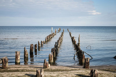 Wooden posts in sea against sky