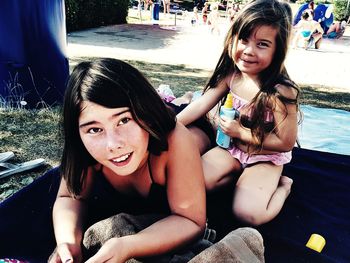 Portrait of smiling young woman and daughter relaxing at poolside