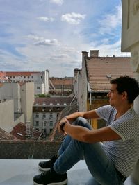 Side view full length of happy man sitting at balcony against buildings
