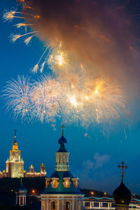 Firework display over illuminated buildings against sky at night