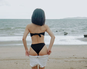 Rear view of healthy body woman standing on beach wearing bikini 