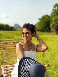 Woman sitting on chair at field against sky