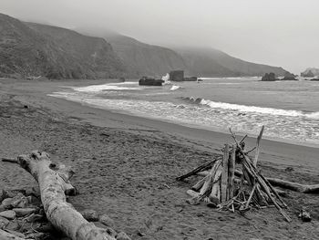 Driftwood structure on ocean beach against cliffs.