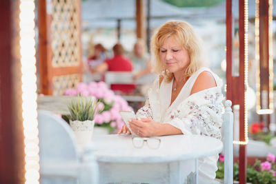 Portrait of young woman using mobile phone while sitting on table