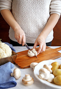 Midsection of woman cutting mushroom on cutting board while standing by table