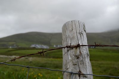 Barbed wire fence on field against sky