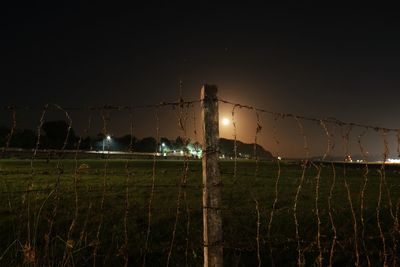 Barbed wire fence on field against sky at night