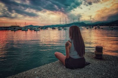 Woman sitting on beach against sky during sunset
