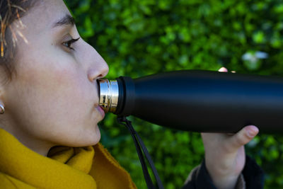 Young woman drinking from a black thermos.