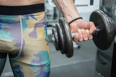 Midsection of man holding dumbbell in gym