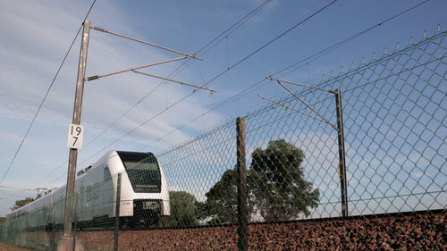 Low angle view of train by fence against sky