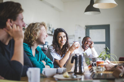 Portrait of cheerful young female computer programmer sitting with hackers at table in creative office