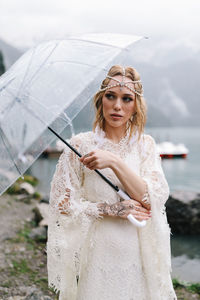 A tender sensual young woman bride in a fashionable wedding dress is standing in the rain in nature