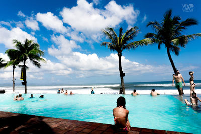 People swimming in pool by sea against sky