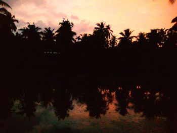 Silhouette trees by lake against sky during sunset