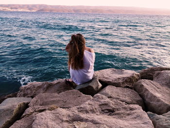 Rear view of woman sitting on rock against sea