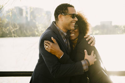 Happy couple embracing while standing by railing against river in city